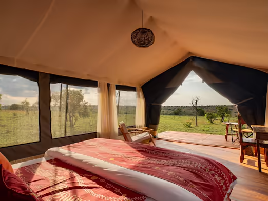 Tented room with a red throw on the bed, opening onto the plains